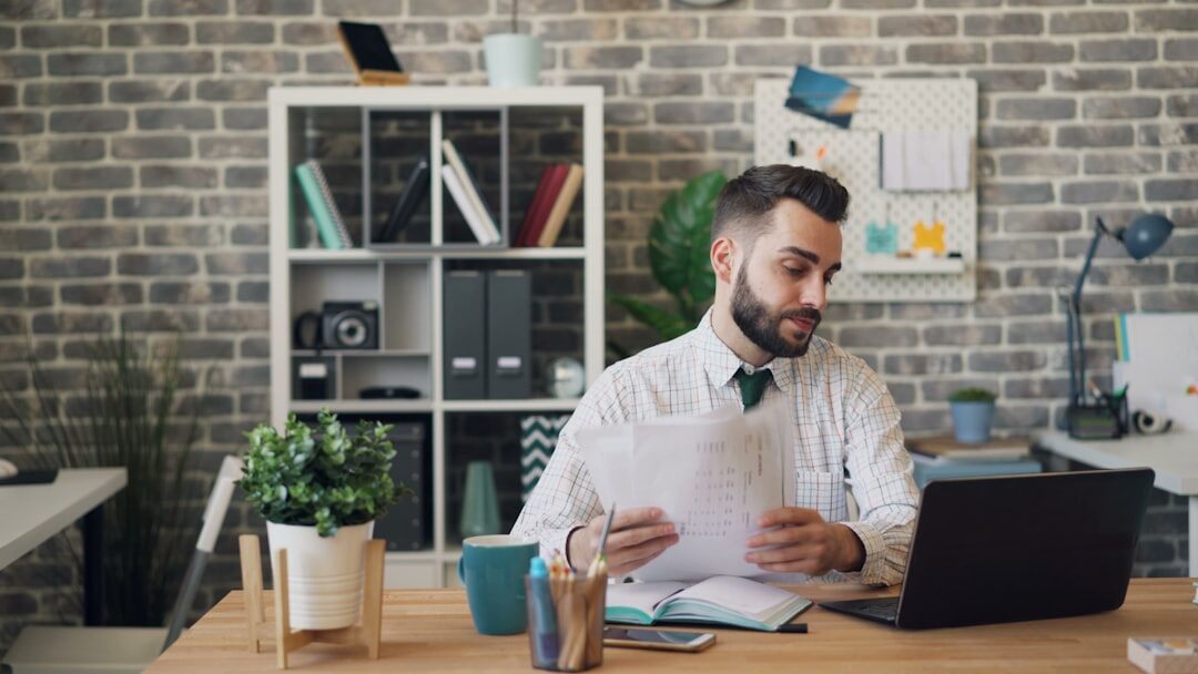 Journalist writing notes at a desk with a laptop and newspapers